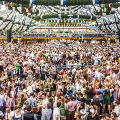 Riesiges Festzelt voller Menschen in Tracht. Die Frage "wie lang geht die Wiesn" beschäftigt viele Besucher dieses Volksfestes.