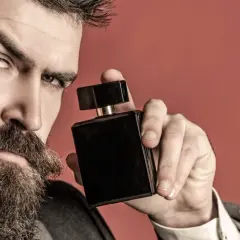 Mężczyzna z brodą trzyma czarną buteleczkę perfum, zastanawiając się, gdzie psikać perfumy, by podkreślić swój styl.