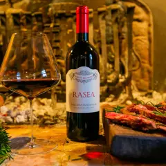 Calice di vino rosso accanto a una bottiglia di Rasea, un vino toscano, con carne grigliata e rosmarino. Un'ode ai super tuscan wines.