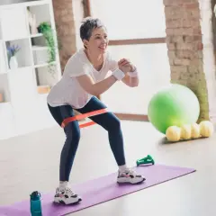 Kobieta ćwiczy w domu, używając taśmy oporowej. To dobry przykład ćwiczeń, których nie trzeba unikać przy osteoporozie.