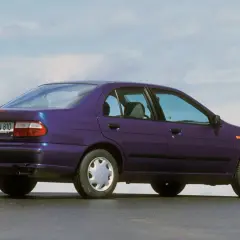 Fioletowy Nissan Almera z lat 90. stoi na tle błękitnego nieba.