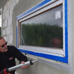 Montaż okien z taśmami rozprężnymi to klucz do energooszczędności. Fachowiec uszczelnia ramę okna.