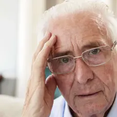 Älterer Mann mit Brille, der sich an die Stirn fasst, wirkt nachdenklich, vielleicht wegen Morbus Korsakow.