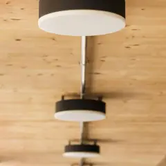 Nowoczesne lampy, każdy plafon ścienny z czarną obudową i białym dyfuzorem, zamontowane na drewnianym suficie.