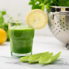 Zielony koktajl ze szpinaku w szklance z plasterkiem cytryny, obok łodygi selera i cytryny.