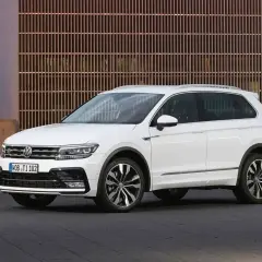 Biały Volkswagen Tiguan 5N z przyciemnianymi szybami i chromowanymi listwami, zaparkowany przed nowoczesnym budynkiem.