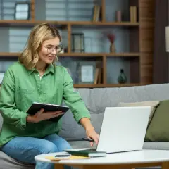 Kobieta na kanapie z laptopem i notatkami uczy się, jak doładować prąd przez internet.