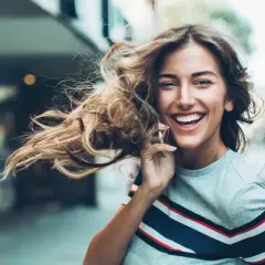 Lachende Frau telefoniert, ihr Haar weht im Wind. Sie genießt ihr **iu auslandssemester** in der Stadt.