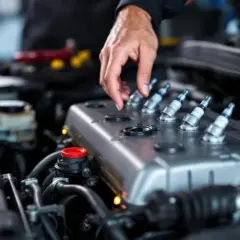 Mécanicien vérifiant les bougies d'allumage d'un moteur essence. Si votre voiture broute en roulant, cela peut venir de là.