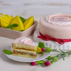 Różowy tort z napisem "Kocham Mamę", udekorowany bielą tytanową spożywczą, obok kawałek ciasta i mango.