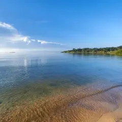 Spokojne, duże jezioro w Afryce, z piaszczystym brzegiem i bujną zielenią w oddali.