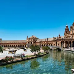 Vacker vy över Plaza de España i Sevilla, Spanien. En hästdragen vagn glider fram längs kanalen under en klarblå himmel.