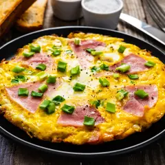 Pyszny omlet z szynką i serem, posypany szczypiorkiem, podany z grzankami. Idealny na śniadanie.