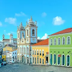 Calles empedradas y coloridas casas coloniales bajo un cielo azul en **Bahía, Brasil**. Una iglesia barroca domina el paisaje.