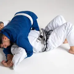 Två män i judodräkter brottas på golvet. En blå och en vit dräkt, en kamp mellan judo vs bjj.