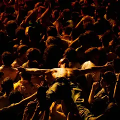 Tłum szaleje w moshpit, unosząc nagiego mężczyznę z rozłożonymi ramionami.