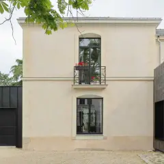 Maison rénovée par un architecte DPLG, mêlant pierre claire, bois sombre et garage noir moderne. Balcon fleuri sur la façade.