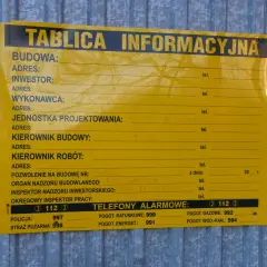 Tablica informacyjna na budowie. Widać pola na dane inwestora, kierownika budowy, numer pozwolenia na budowę i telefony alarmowe. Ważne jest pozwolenie na budowę, by wszystko było legalne.