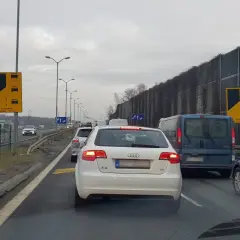 Korek na drodze, samochody stoją w miejscu. Widoczny znak "Zalecana zasada ruchu" informujący o konieczności stosowania jazdy na suwak.