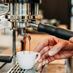 Frisch gebrühter Espresso fließt aus der Maschine in eine kleine Tasse. Die Zubereitung von handgebrühtem Kaffee ist ein Kunstwerk.
