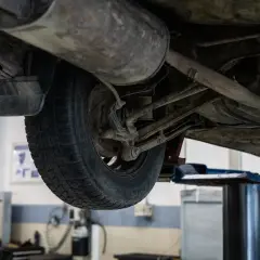 Vista inferior de un coche en elevador, listo para alineación y balanceo. Se aprecian el neumático, suspensión y escape.