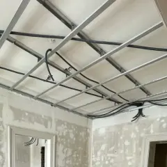 Structure métallique pour faire un faux plafond, avec des câbles électriques en cours d'installation. Les murs sont en chantier.