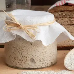 Słoik z zakwasem, gotowy do pieczenia chleba. Obok kromki pysznego, lekko lepkiego w środku chleba.