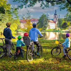 Rodzina na rowerach podziwia jesienny krajobraz krainy Górnej Odry. W tle pałac i jezioro.