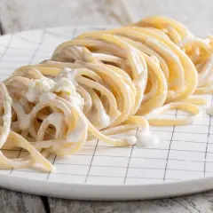 Un piatto di spaghetti avvolti in una cremosa salsa alla panna, serviti su un piatto bianco a quadretti neri.