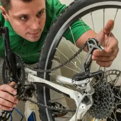 Mężczyzna w zielonej koszulce dokonuje renowacji roweru, pracując przy przerzutce i łańcuchu.
