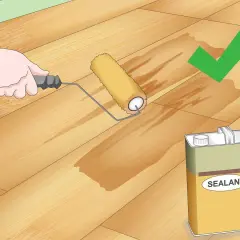 Application d'un scellant sur un plancher en bois. Le rouleau laisse une trace humide, signe que le produit pénètre bien le bois, éliminant toute rayure.