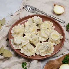 Smażone pierogi z mięsem na brązowym talerzu, z cebulą i natką pietruszki w tle.