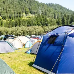 Pole namiotowe pełne kolorowych namiotów, w tym niebieski namiot do plecaka, na tle zielonych wzgórz.