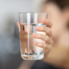 Main d'une personne tenant un verre d'eau. L'eau calcaire peut affecter la santé, mais une hydratation adéquate est essentielle.