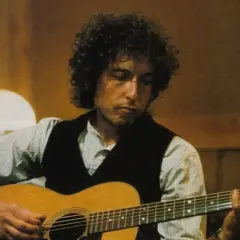Bob Dylan gra na gitarze, tworząc ponadczasowe utwory.