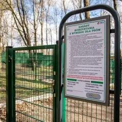 Zielona brama do parku dla psów, z tablicą informującą o zasadach korzystania.