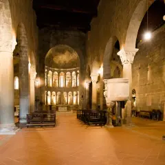 Interno della pieve di Gropina, con colonne massicce, archi in pietra, un pulpito scolpito e l'abside illuminata.