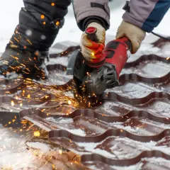 Praca przy wymianie dachu w zimowych warunkach. Iskry sypią się spod szlifierki tnącej blachodachówkę.