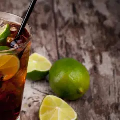 Erfrischender Cuba Libre mit Limettenspalten und Eiswürfeln auf rustikalem Holz. Das Cuba Libre Rezept ist einfach und lecker.