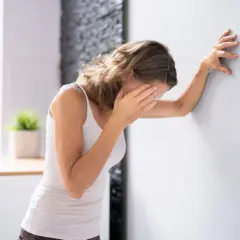 Frau lehnt sich an Wand, hält sich die Augen. Sie fragt sich, was tun bei Schwindel.