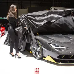 Elegancki mężczyzna i dwie kobiety odsłaniają nowy, szary Lamborghini Centenario. Obok stoi czerwony sportowy samochód.