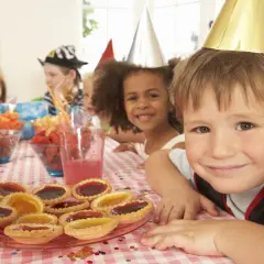 Glada barn med kalashattar vid ett dukat bord med tårtor och frukter. Perfekt för kalaslekar 5 år!