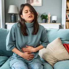 Frau mit Bauchschmerzen auf dem Sofa, die sich fragt, was essen bei Periode.