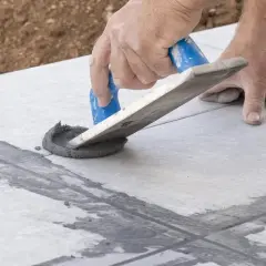 Hand arbeitet mit Spachtel, um graue Masse in Fliesenfugen zu verteilen. Präzises fliesenfugen abdichten für ein perfektes Ergebnis.