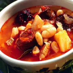 Un reconfortante plato de alubias con chorizo, trozos de patata y carne en un caldo rojizo.