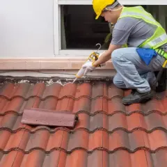 A roofer applies sealant to a shingle roof detail, ensuring a watertight seal around the window.