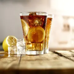 Dwa orzeźwiające drinki Long Island Ice Tea z plasterkami cytryny i kostkami lodu na drewnianym blacie.
