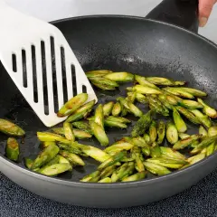 Geschnittener Spargel brät in einer Pfanne. Ein weißer Pfannenwender bewegt die grünen Stücke.