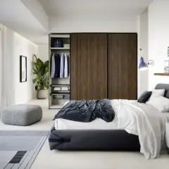Elegante camera da letto piccola con letto matrimoniale, armadio a muro in legno scuro, pouf e tappeto grigio.