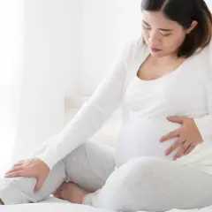 Schwangere Frau mit Hand auf dem Bauch und Bein, die Beschwerden oder Kompression während der Schwangerschaft andeutet.